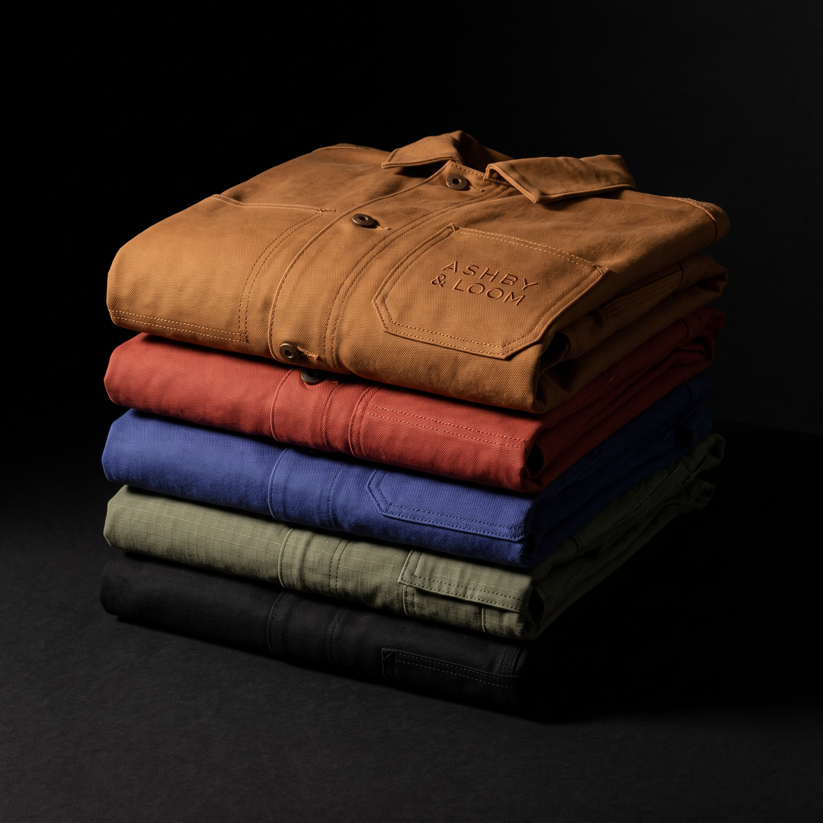 ASHBY & LOOM — pile de vestes et pantalons en toile pliés, marque brodée ton sur ton